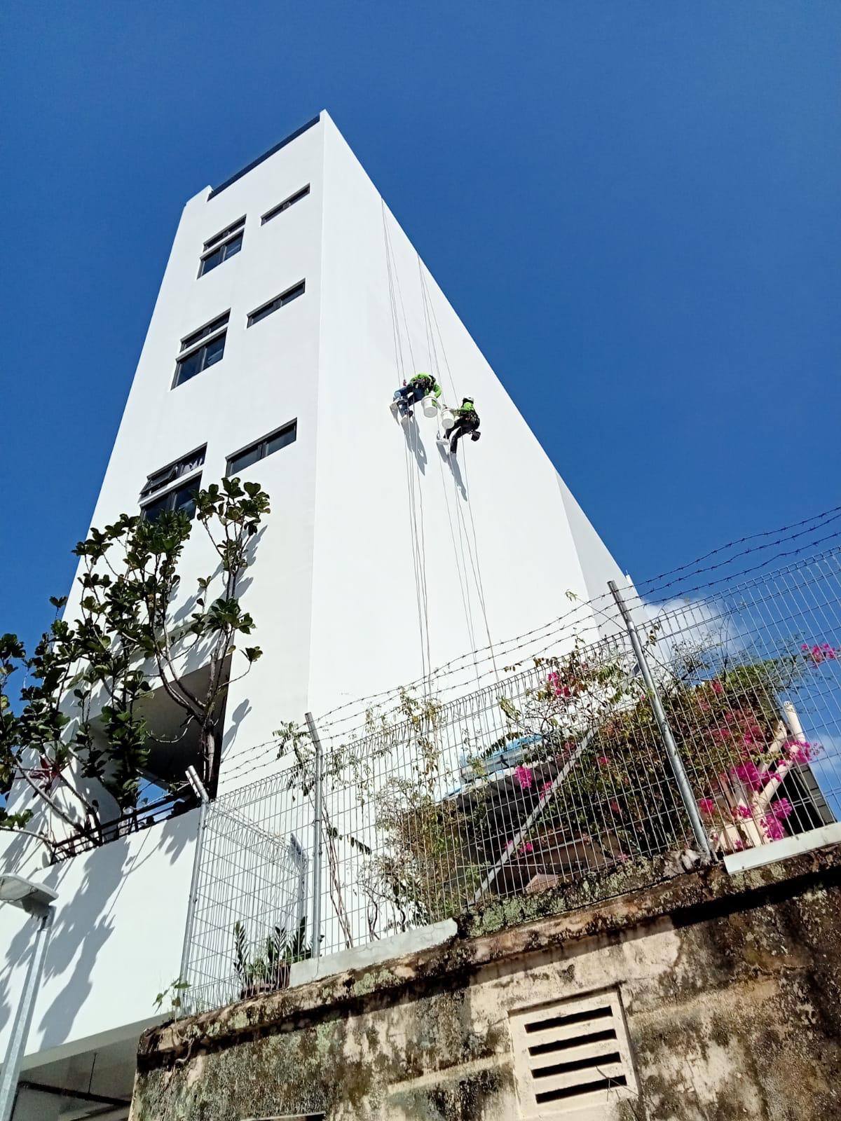 Two rope access technicians on twin ropes treating a spalled concrete edge on a high-rise HDB block facade in Bedok South, Singapore