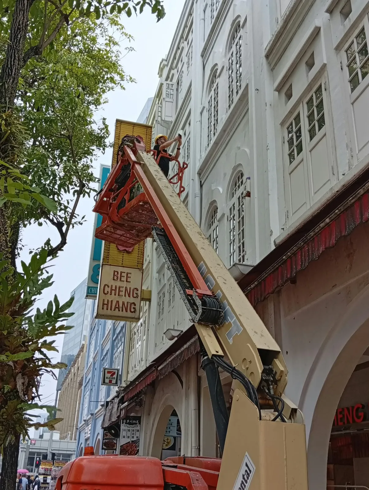 Worker in a boomlift basket at the upper façade of the shophouse