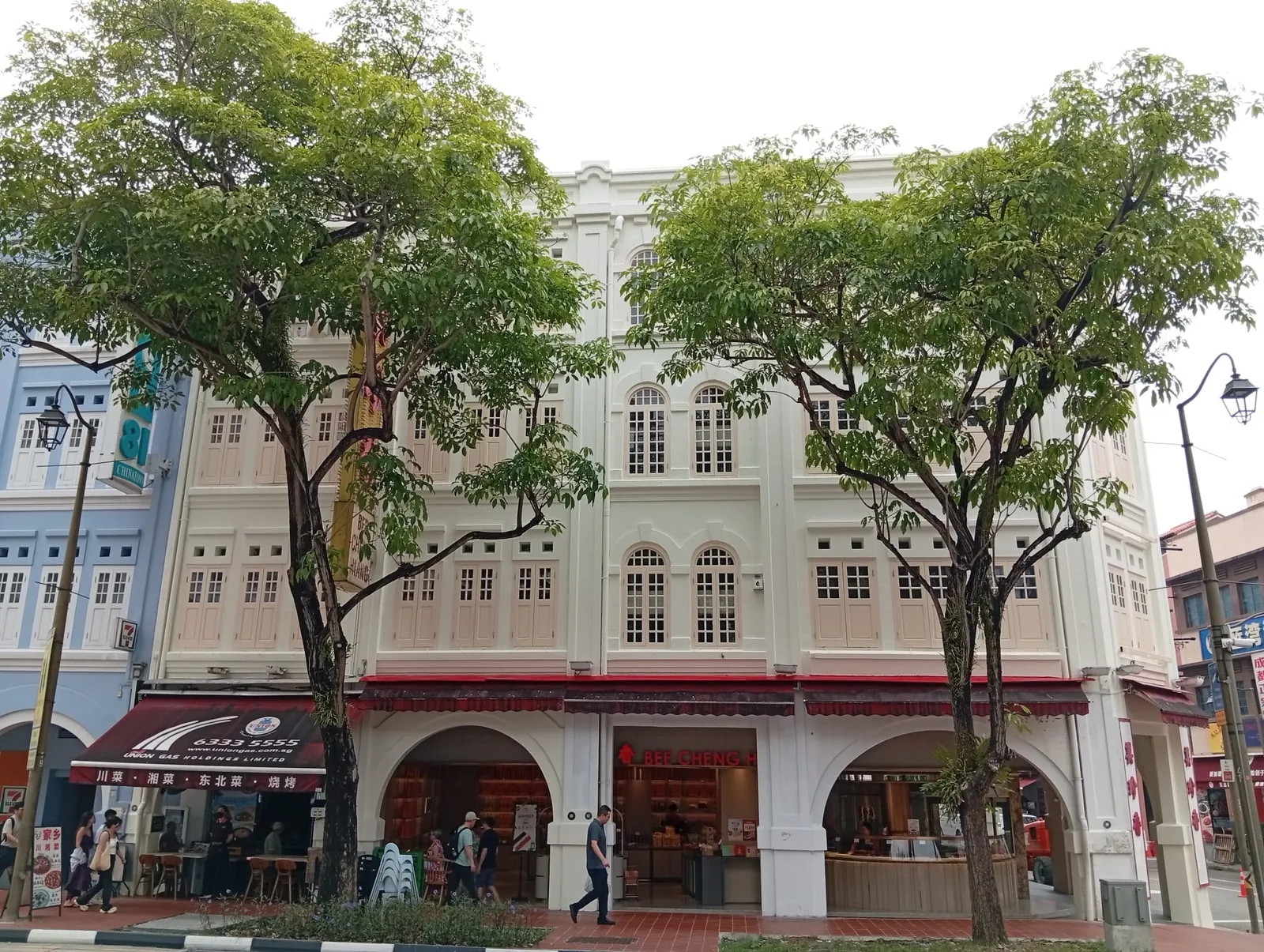 Restored heritage shophouse façade at 189 New Bridge Road, with cream walls, arched windows and timber shutters behind street trees