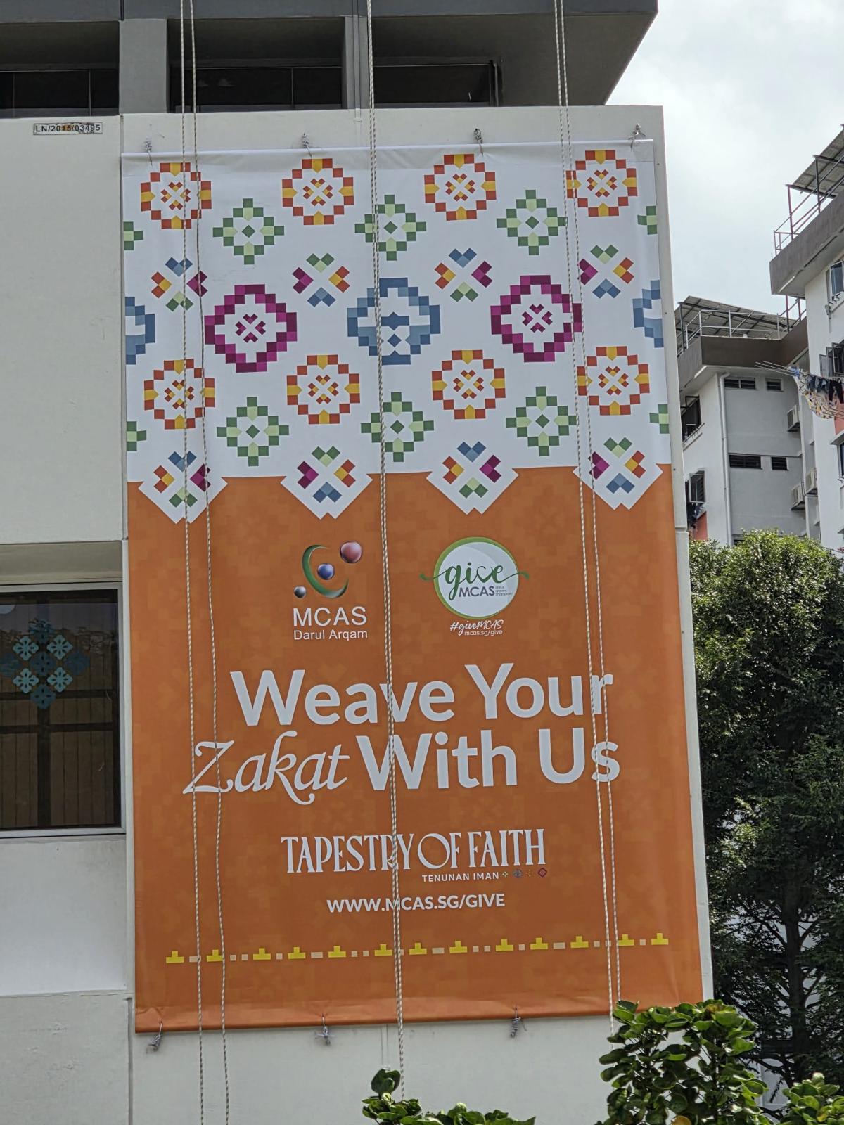 Close-up of the finished MCAS Zakat Tapestry of Faith banner installed on the building elevation showing the full campaign artwork and URL