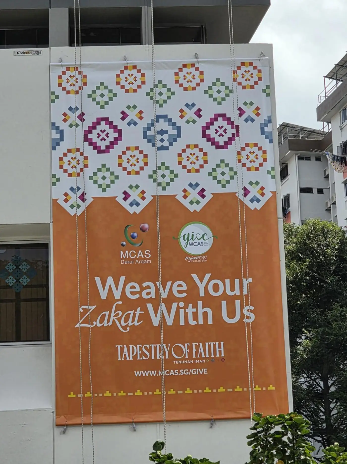 Close-up of the finished MCAS Zakat Tapestry of Faith banner installed on the building elevation showing the full campaign artwork and URL