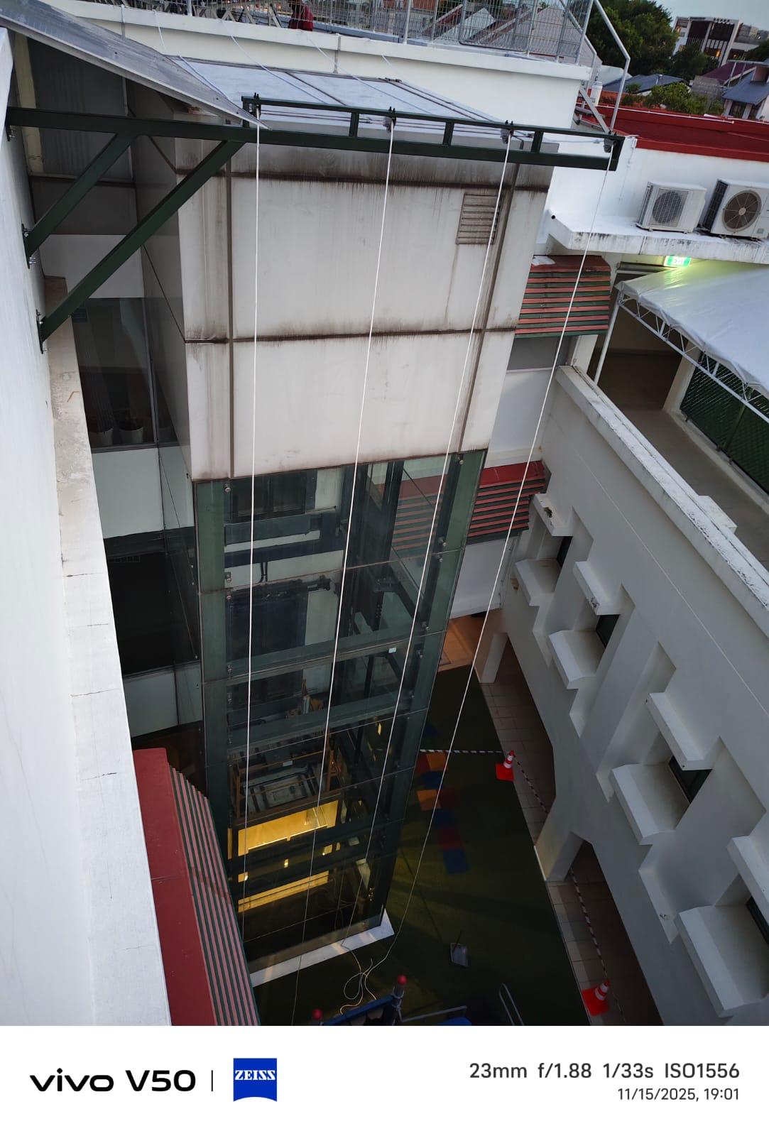 Second elevation view of the same glass lift shaft showing the steel cantilever support bracket and rope access rigging in position for banner display