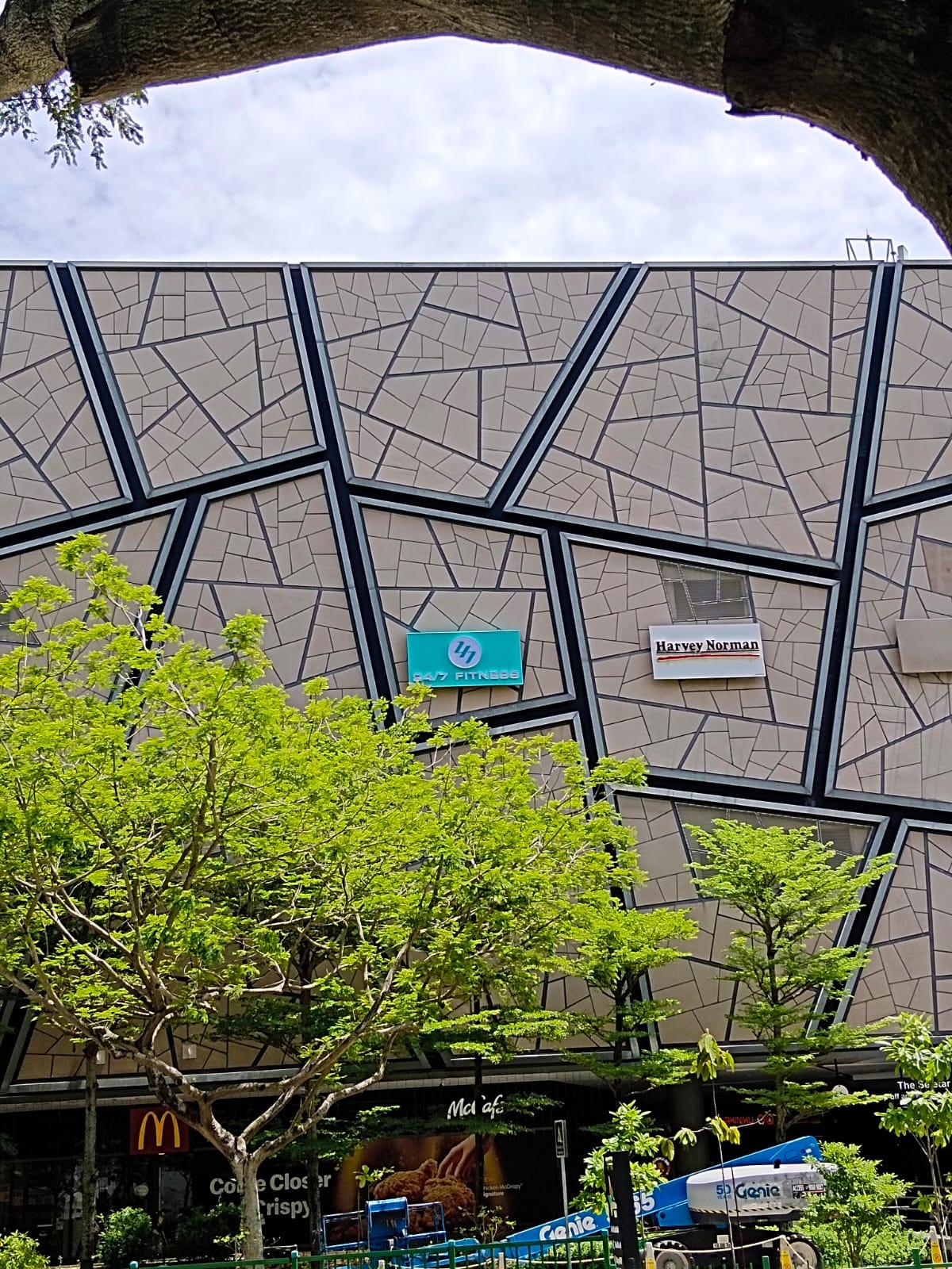 Wider context view of The Seletar Mall facade with the new tenant signage in position and a boomlift visible at the base for coordinated access