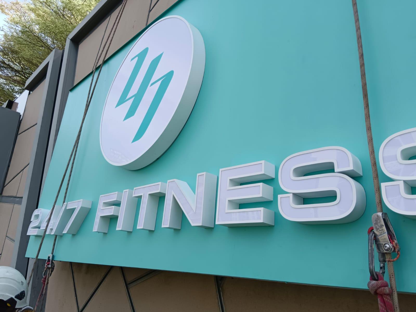 Close-up of installed fitness signage on The Seletar Mall tiled facade with rope access lines and a technician helmet visible at the lower frame